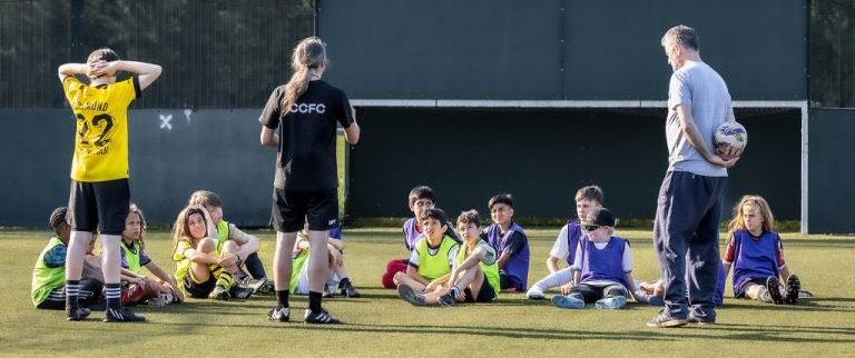 Kids sit on pitch, listening to CCFC coaches